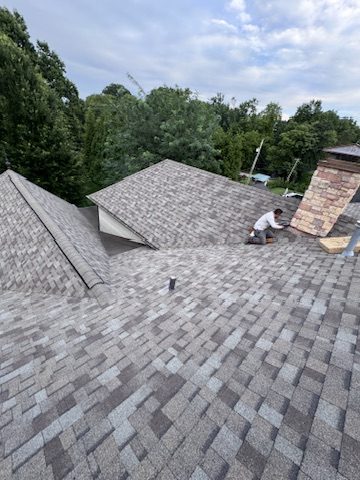 Crew member installing architectural shingles near a chimney